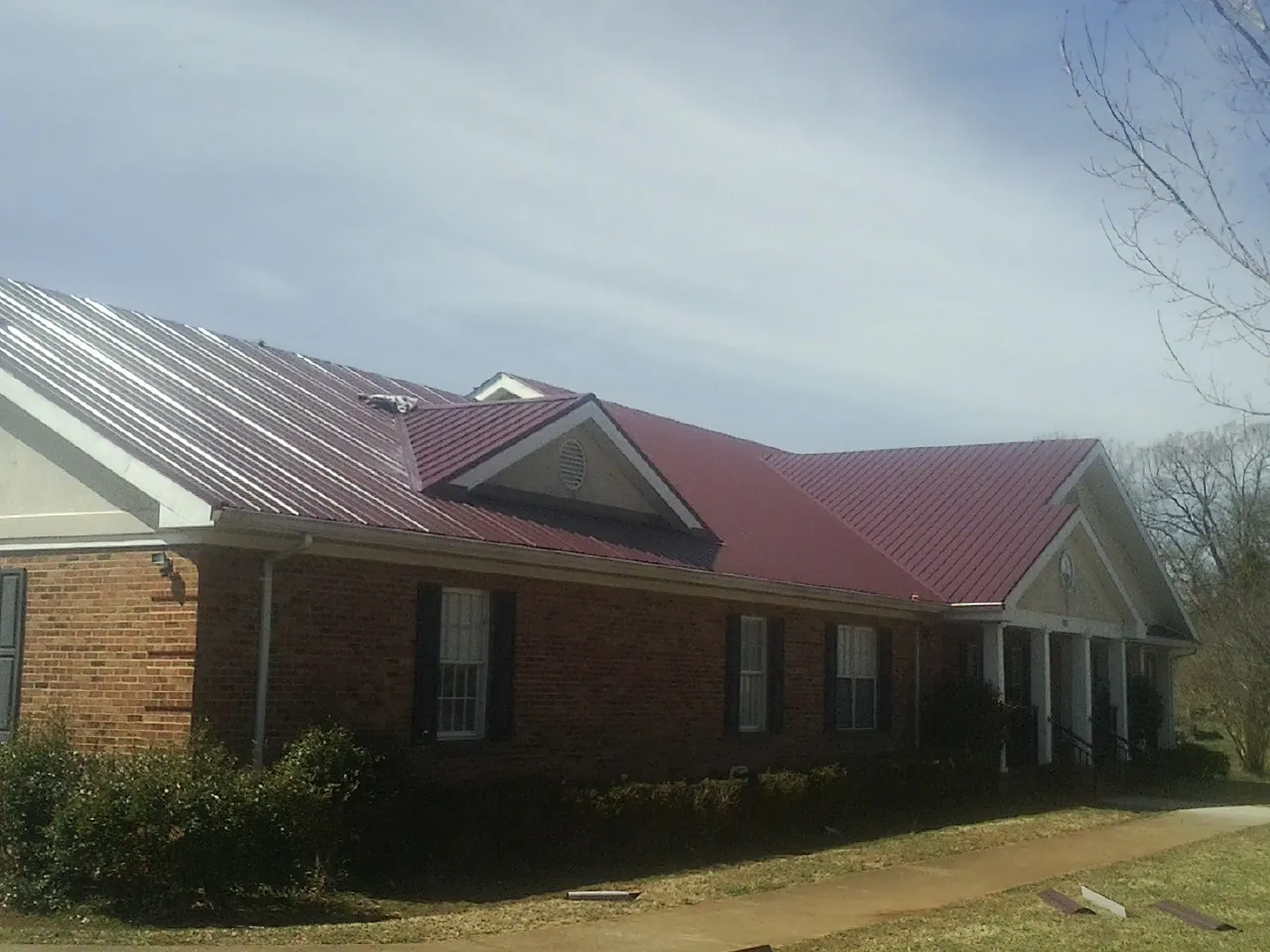 Red metal roof with gabled entries on a long brick building, from a Hail Damage Roof Repair job in Huntley
