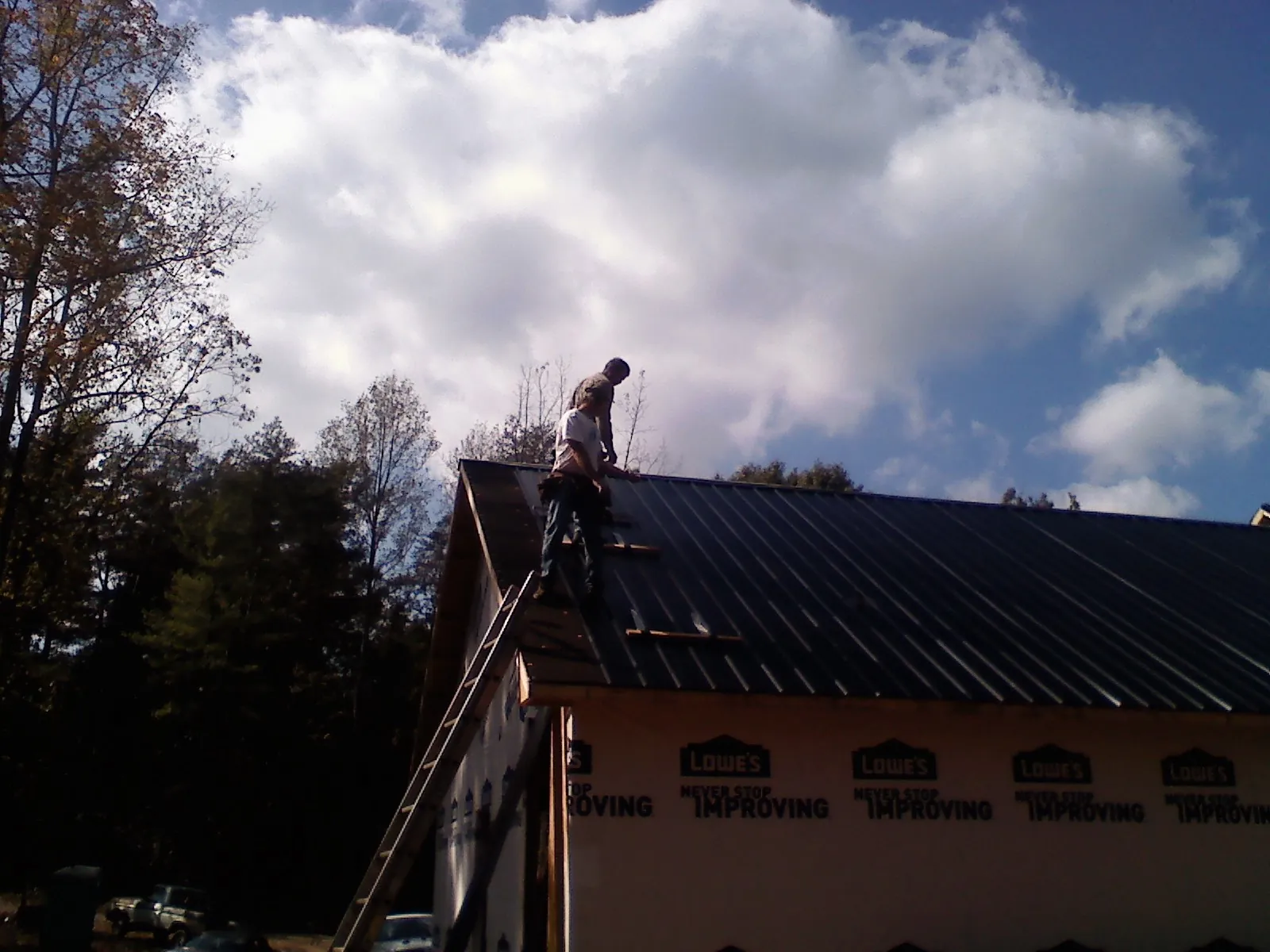 Roofer fastening dark metal panels high against a cloudy sky, from a Roof Inspection job in Huntley