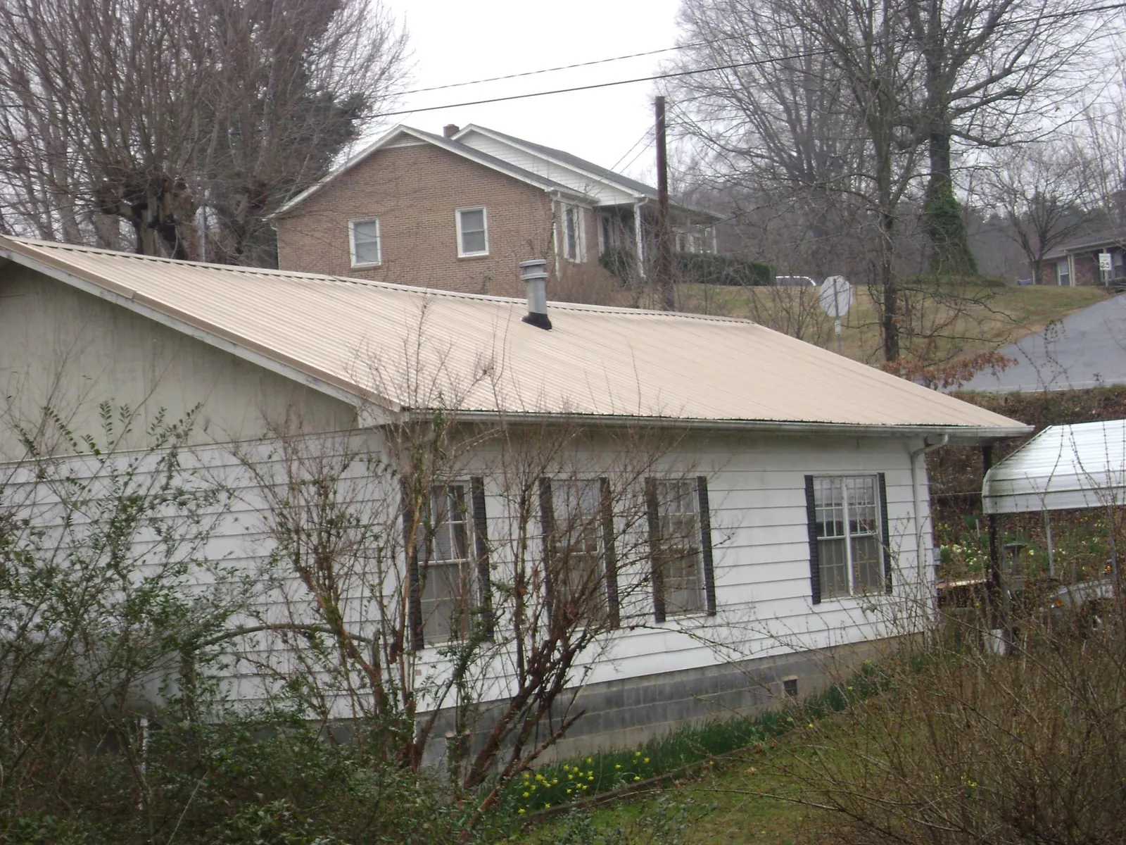 Tan metal roof on a white sided house set into a hillside — Commercial Roofing by Roofing Brothers in Huntley